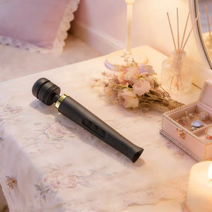 Black wand massager displayed on a bedside table in a lifestyle setting