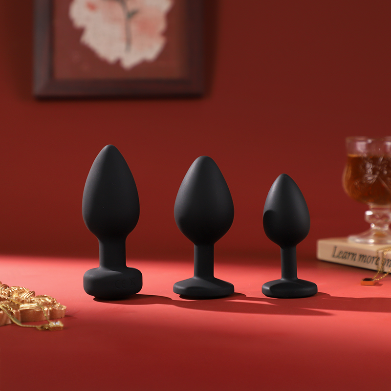 Three black silicone butt plugs on a red surface with a blurred background